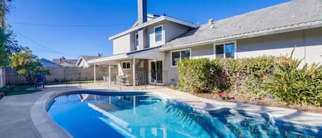 A residential property with a swimming pool, a covered patio, and a two-story house.