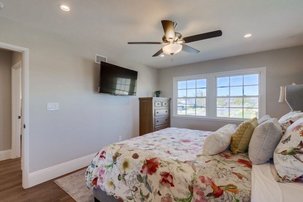 A bedroom with a bed, a ceiling fan, a window, and a television on the wall.