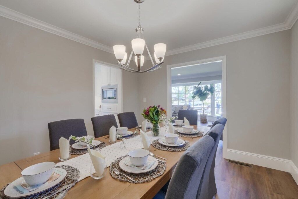 Comedor con una mesa de madera dispuesta para seis personas, rodeada de sillas, una araña y vistas al exterior.