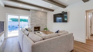 A living room with a sectional sofa, a fireplace, a flat-screen TV, and a large window.