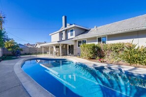 Una propiedad residencial con piscina, un patio cubierto y una casa de dos pisos.