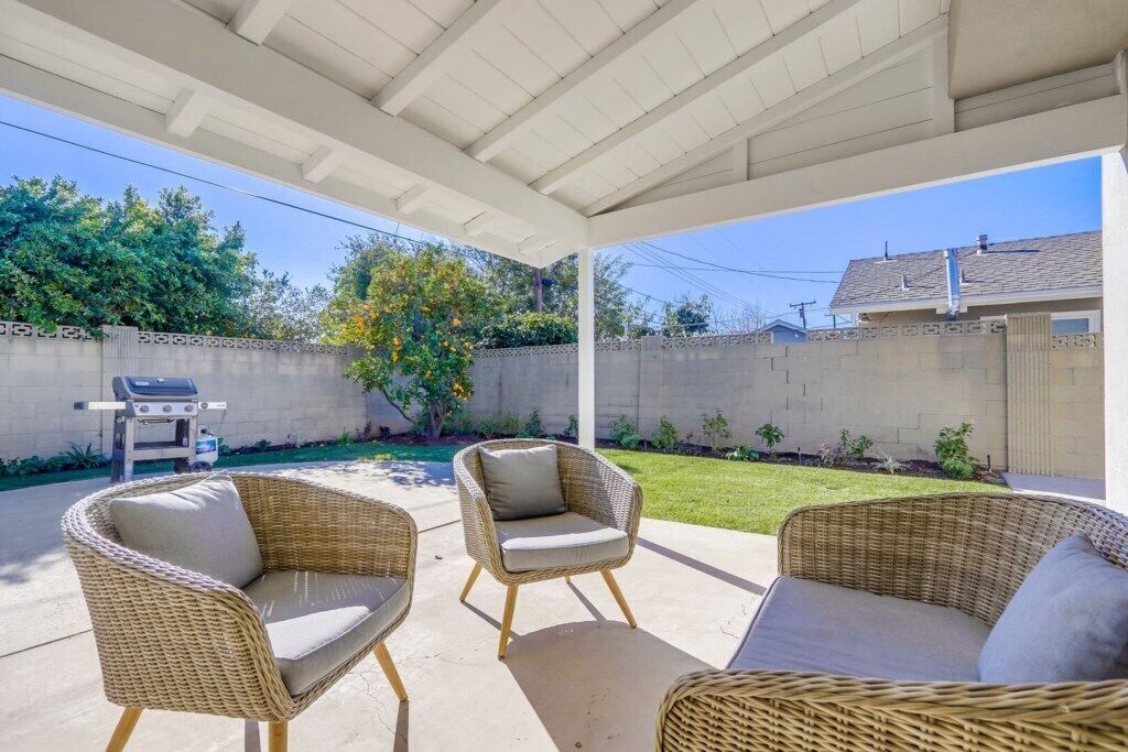 A covered patio with wicker furniture, a grill, and a view of a backyard.