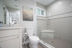 A bathroom with a toilet, a shower, a sink, and a mirror.