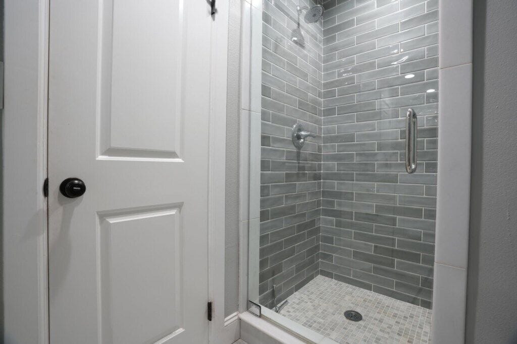 Une douche fermée par des parois de verre, avec un sol carrelé et une porte blanche.
