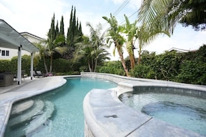 A swimming pool with a curved design, surrounded by palm trees and a covered patio area.