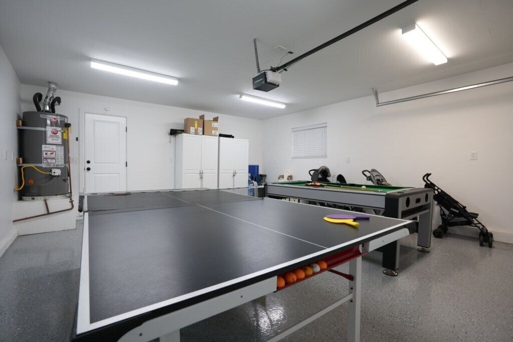 Ett bordtennisbord i ett rum med en projektor, ett biljardbord och en värmare.