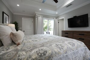 A bedroom with a large bed, a TV, a dresser, and a view of the outdoors.