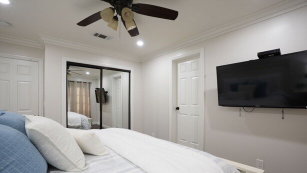 A bedroom with a bed, a ceiling fan, a TV mounted on the wall, and a door leading to another room. - Stunning 5 Bedroom, 3 Bath Home 1/2 Mile Walk To Disney (Anaheim)