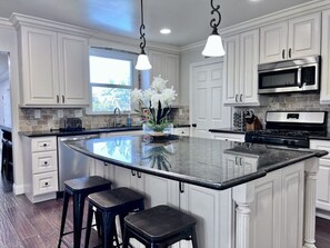 Una cocina con gabinetes blancos, una isla grande con taburetes, un microondas y una estufa.