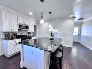 A kitchen with white cabinets, a black granite countertop, a stainless steel oven, and a pendant light. - Stunning 5 Bedroom, 3 Bath Home 1/2 Mile Walk To Disney (Anaheim)