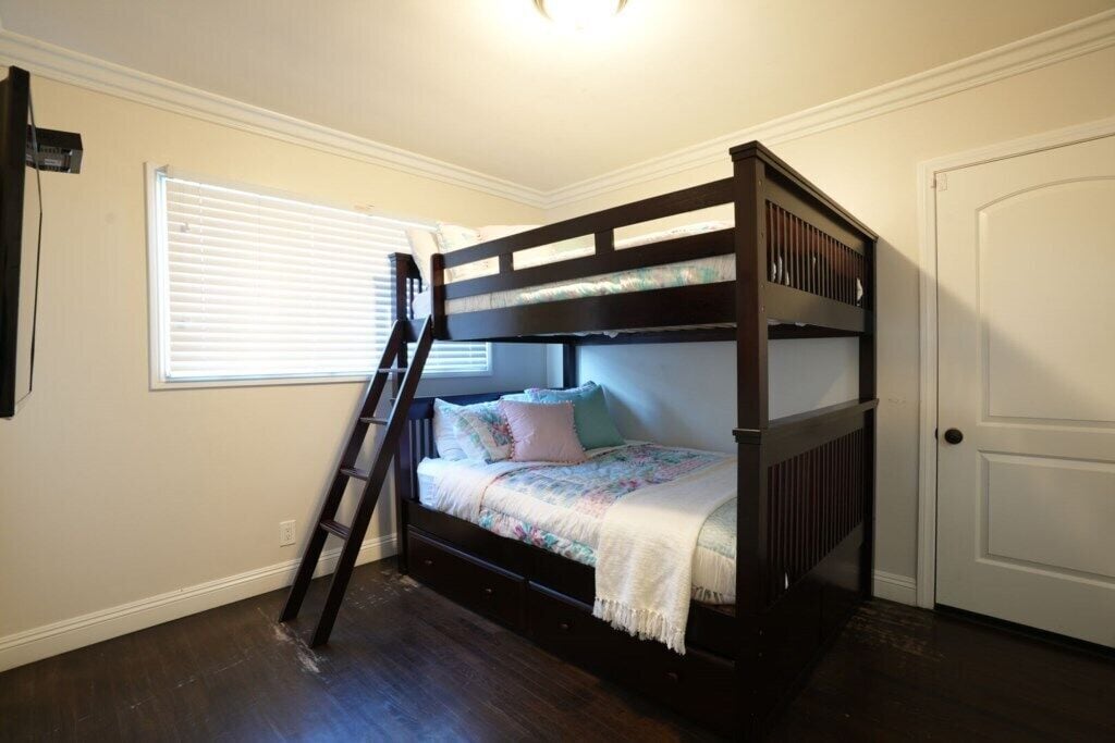 A bunk bed with a ladder, a window with blinds, and a door.