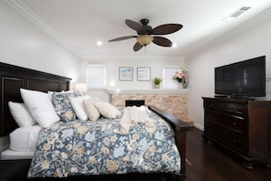Une chambre à coucher comprenant un lit, un ventilateur de plafond, une cheminée, un téléviseur et une commode.
