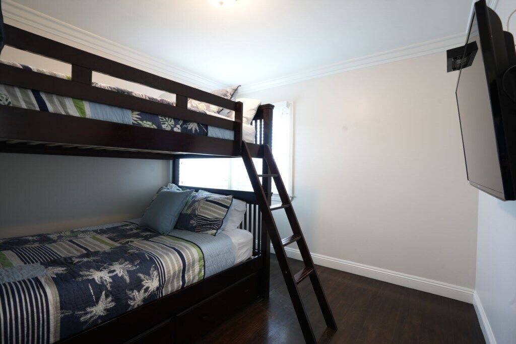 Una cama litera con escalera, una ventana y un televisor en la pared.