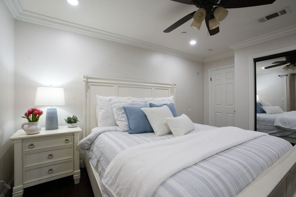 A bedroom with a bed, nightstand, lamp, and ceiling fan.
