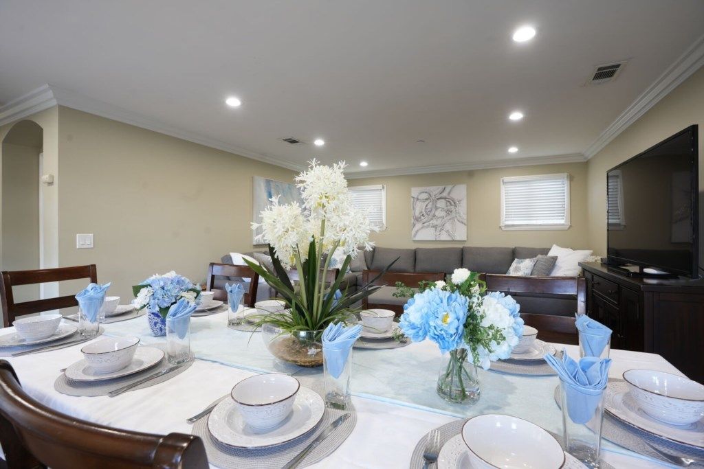 Un comedor con una mesa redonda dispuesta para seis personas, rodeada de sillas. Hay jarrones decorativos con flores sobre la mesa.