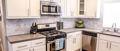 A modern kitchen with white cabinets, a stainless steel stove, a microwave, and a dishwasher.
