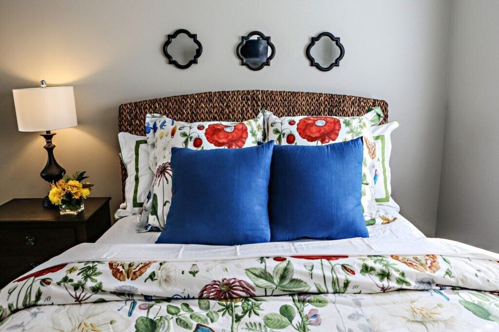 A bed with floral bedding, a bedside lamp, and decorative mirrors on the wall.