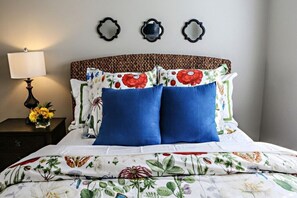 Un lit avec une literie à motifs floraux, une lampe de chevet et des miroirs décoratifs accrochés au mur.