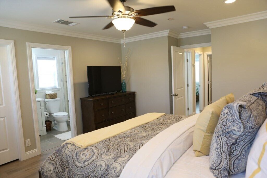 A bedroom with a bed, a dresser, a television, and a ceiling fan.