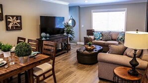 Een woonkamer met een televisie, bank, eettafel, stoelen en een lamp.