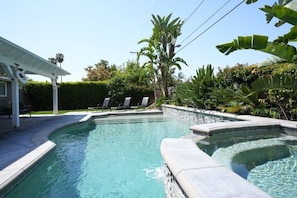Una piscina de borde curvo, rodeada por una terraza de piedra y un área de patio techada con sillones de descanso.
