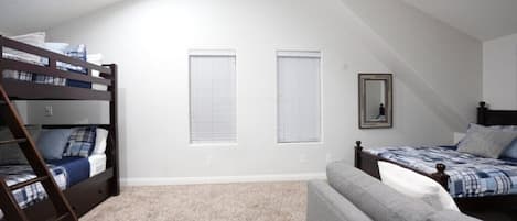 A bedroom with bunk beds, a sofa, two windows, and a mirror.