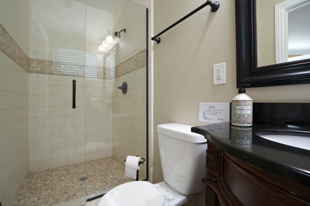 A bathroom with a glass shower enclosure, a toilet, and a sink with a mirror above it.