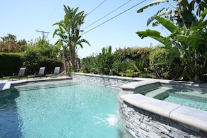 A swimming pool with stone walls, surrounded by lush greenery and a clear sky. - Sweet 4 bedroom, 3 bath plus Loft Bedroom, Pool Home (Anaheim)