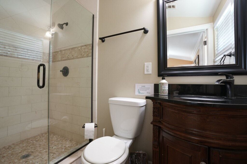 A bathroom with a glass-enclosed shower, a white toilet, a wooden vanity, and a mirror.