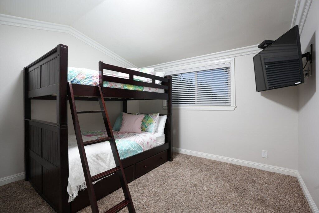 Een stapelbed met een ladder, een raam met zonwering en een airconditioner aan de muur in een slaapkamer.