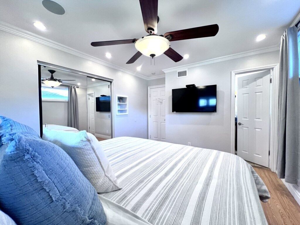 Een slaapkamer met een bed, plafondventilator, televisie en een deur.