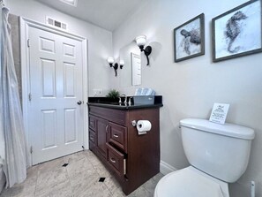 Une salle de bain avec des toilettes blanches, un meuble-lavabo en bois foncé, un miroir, des appliques murales et deux tableaux encadrés représentant des hippocampes.