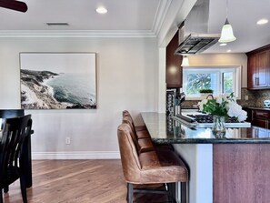 Une cuisine dotée d’un grand îlot central, de tabourets de bar, d’un luminaire suspendu et d’un tableau représentant un paysage marin accroché au mur.