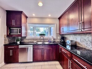 A kitchen with dark wood cabinets, stainless steel appliances, a window, and a brick backsplash. - Cute 3 Bedroom 2 Bath Home Near Convention Center & Disney (Anaheim)