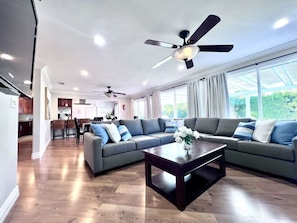 Ein modernes Wohnzimmer mit Ecksofa, Couchtisch, Deckenventilatoren und großen Fenstern.