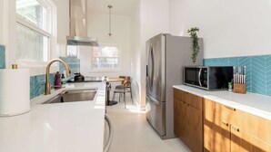 A modern kitchen with a stainless steel refrigerator, a microwave, and a sink. There is a window providing natural light and a plant on the countertop. - Mid-Century Dream | 3BR/2BA | Heart of Hawthorne (Portland)