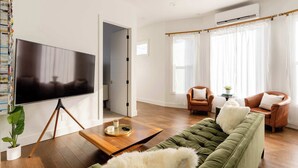A modern living room with a flat-screen TV, a green sofa, two leather armchairs, and a wooden coffee table. - Mid-Century Dream | 3BR/2BA | Heart of Hawthorne (Portland)