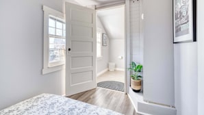 A bedroom with a bed, a door leading to a hallway, a window, and a framed picture on the wall.