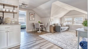 A spacious loft with a high ceiling, a dining area with a round table and chairs, a cozy seating area with a sofa, and a kitchen with shelves and a countertop.