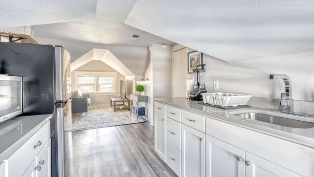 A modern kitchen with a large island, stainless steel appliances, and a view into a living area with a high ceiling and skylight.