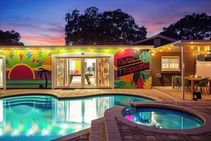 A pool area with a sunset mural, a Tropical-themed restaurant, and a poolside seating area. - Electric Tropicana! Pickleball, Mini Golf, Pool (Seminole)