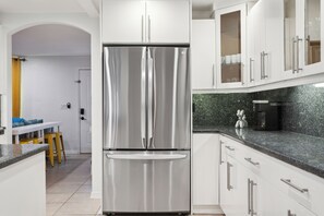 Enjoy cooking in this well-equipped kitchen with a stainless steel refrigerator, white cabinetry, and granite countertop.