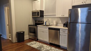A compact kitchen with white cabinets, stainless steel appliances, and a black trash bin. - Mellow ☮ BnB, a NEW 3/1.5 in Victorian District (Savannah)