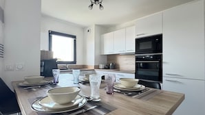 A modern kitchen with white cabinets, a wooden dining table set with bowls, plates, and cutlery, and a black oven.