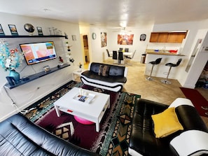 A living room with a TV, sofa, coffee table, and a dining area with chairs and a table.
