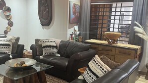 A living room with a brown leather sofa, a glass coffee table, and a hanging light fixture.