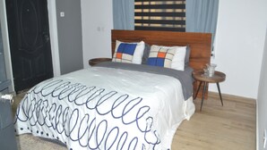 A bedroom with a bed, a wooden headboard, a bedside table, and a small table with a lamp.