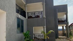 A modern building with two balconies, each with a geometric black railing, and a concrete courtyard with potted plants.