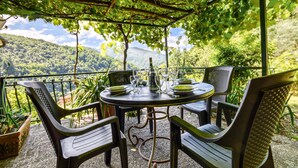 A table set for four with a bottle and glasses, surrounded by chairs, under a pergola with a view of a mountainous landscape. - 1 bedroom lovely apartment in Mezzanego (Mezzanego)