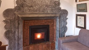 A fireplace with intricate carvings, a brick surround, and a lit fire. - 1 bedroom lovely apartment in Mezzanego (Mezzanego)